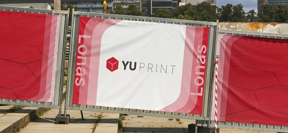 Lona publicitaria personalizada YUPrint instalada en valla metálica para señalización exterior.
